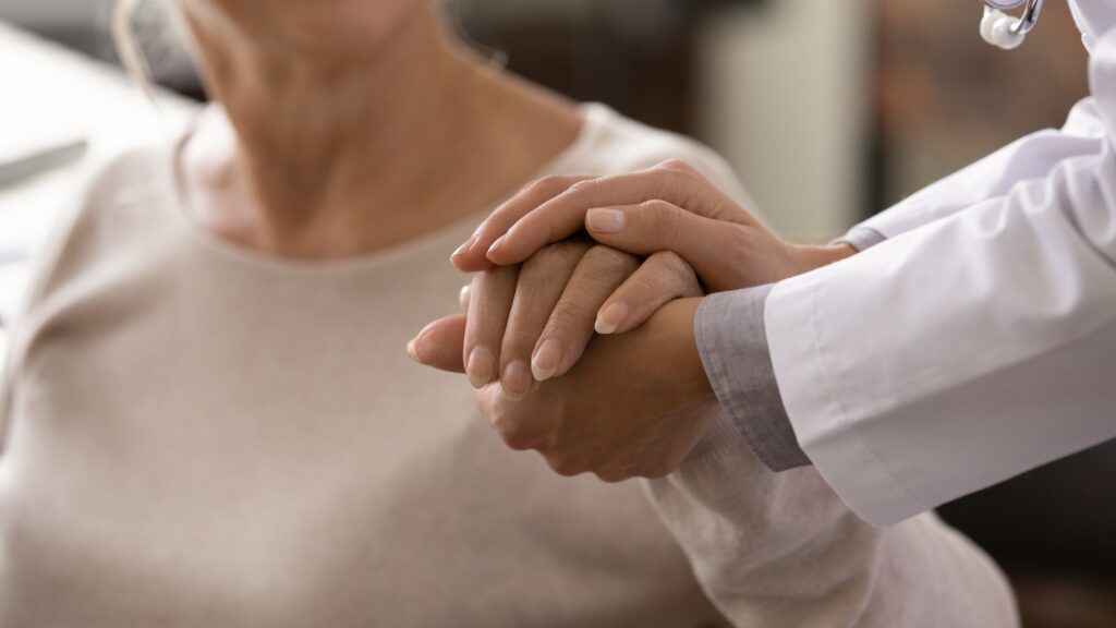 Doctor in a white coat holding a patient's hands in comfort